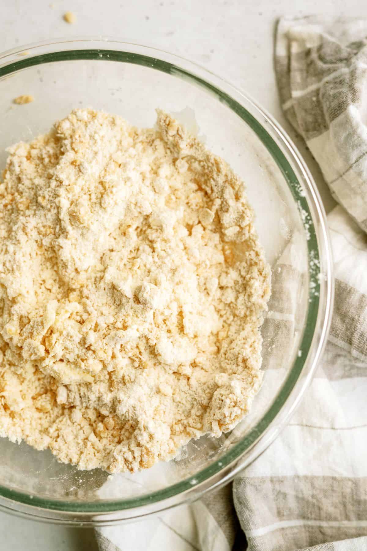 A glass bowl with a crumble mixture from shortening and dry cereal mixture.