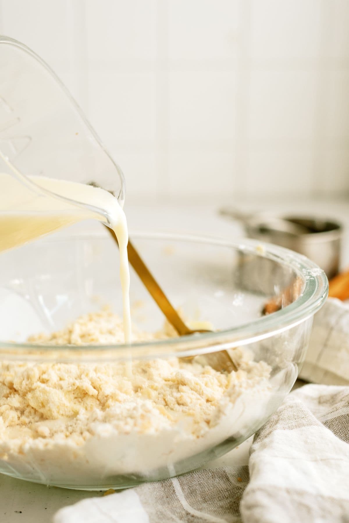 Pouring milk into a glass mixing bowl with the crumble mixture.