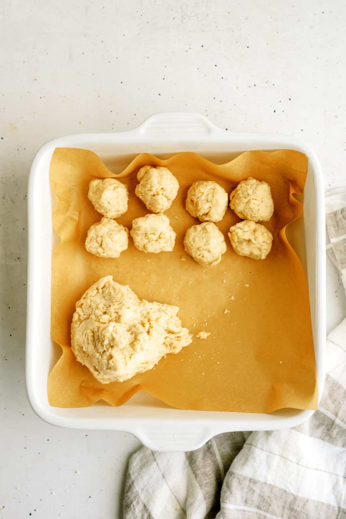 One inch balls of doug in a baking dish lined with parchment paper with a large dough ball.