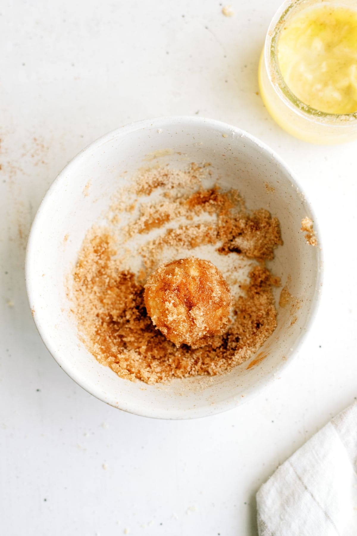 An unbaked dough ball rolled in a small dish of cinnamon and surger mixture.