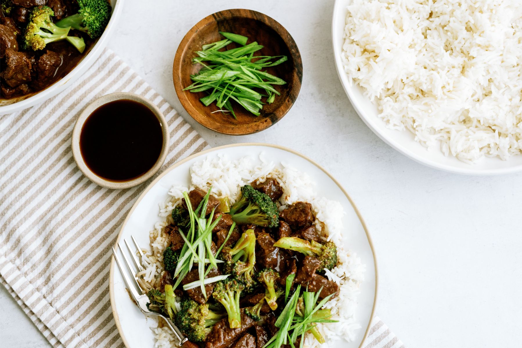 Plate of Instant Pot Beef and Broccoli with a bowl of rice and soy sauce 