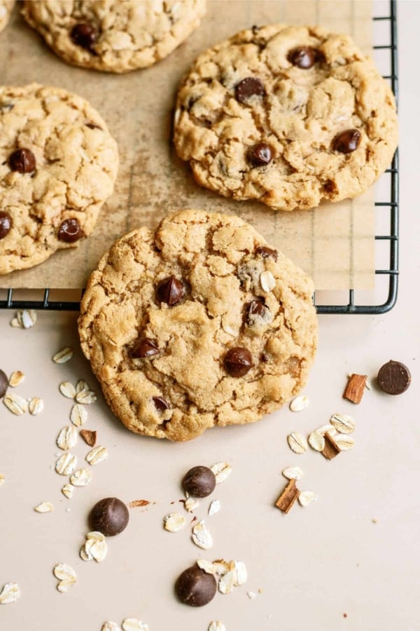Oatmeal Chocolate Chip Peanut Butter Cookies on a parchment line cooling rack with one cookie leaning off the rack.