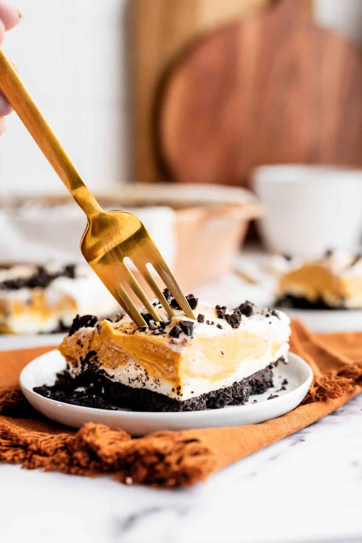 A fork taking a bite out of a slice of Oreo Pumpkin Delight on a plate