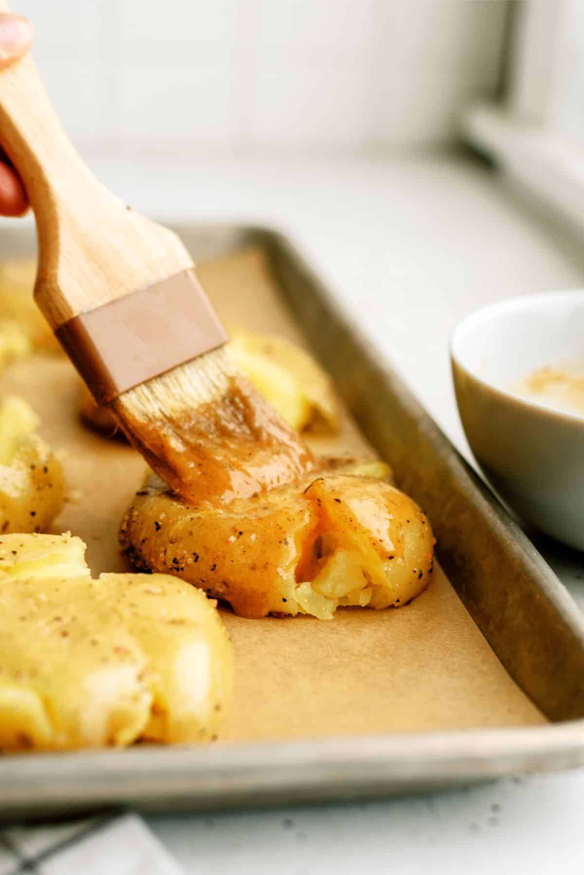 Using a pastry brush to put butter on smashed potatoes