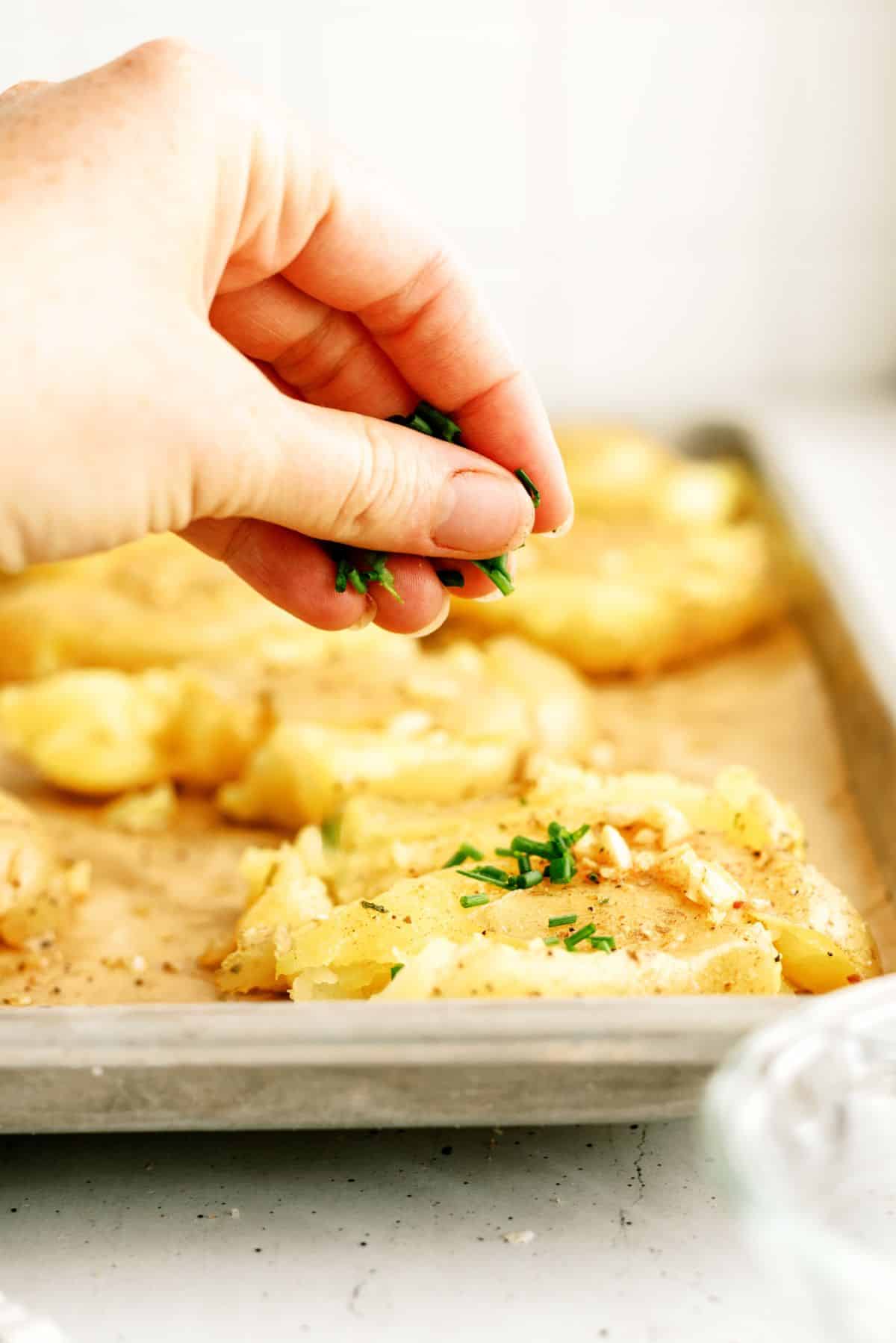 Sprinkling chives on Smashed Cheesy Potatoes