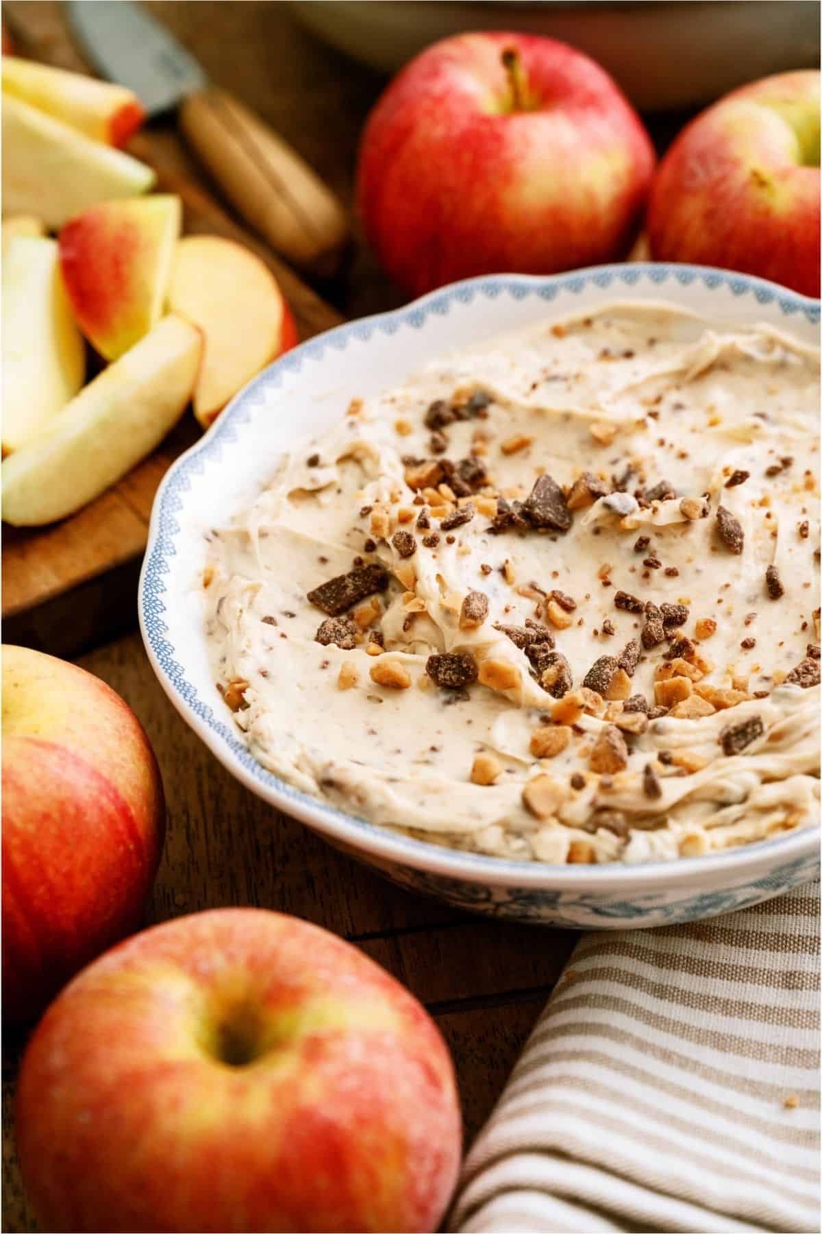 A bowl of Toffee Apple Dip with sliced apples and whole apples around it.