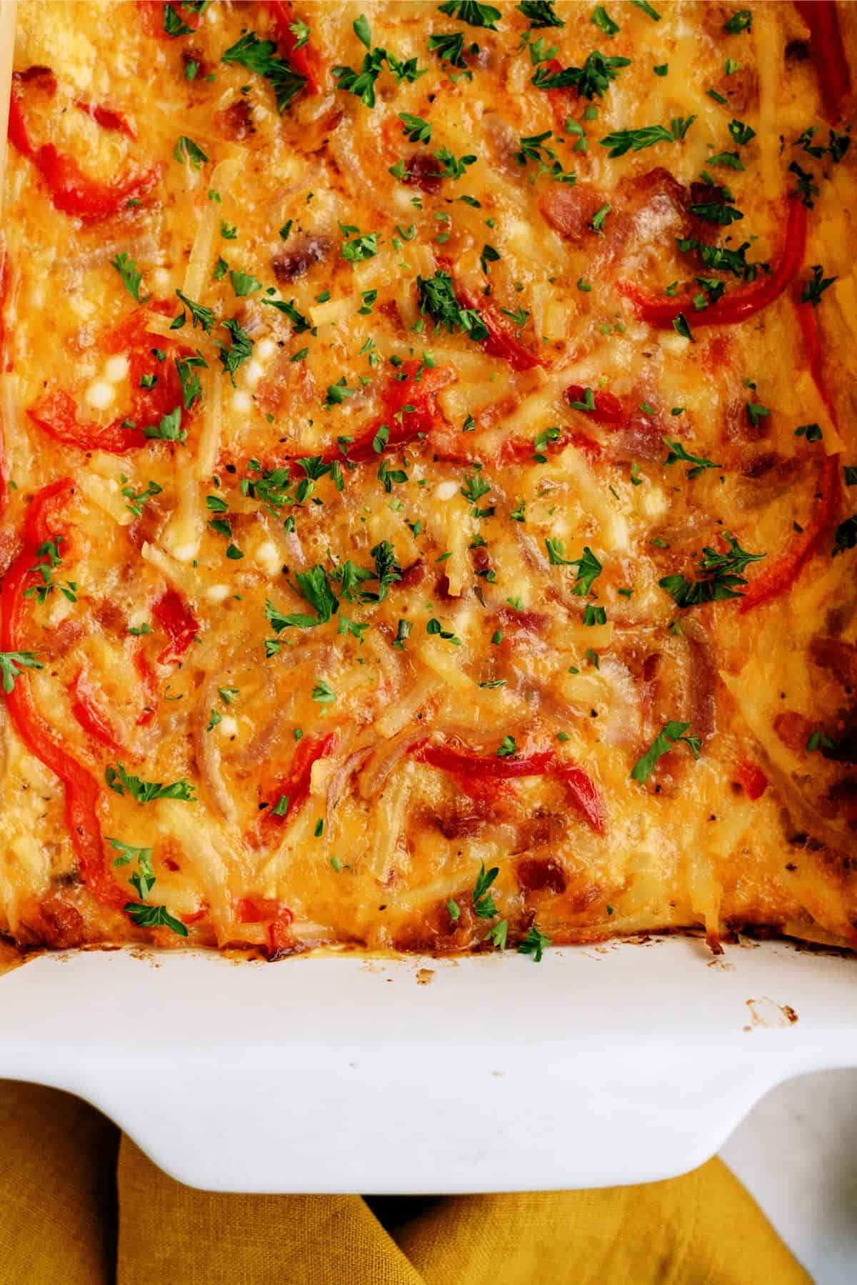 Baked cheesy casserole topped with red bell peppers and chopped parsley in a white dish.