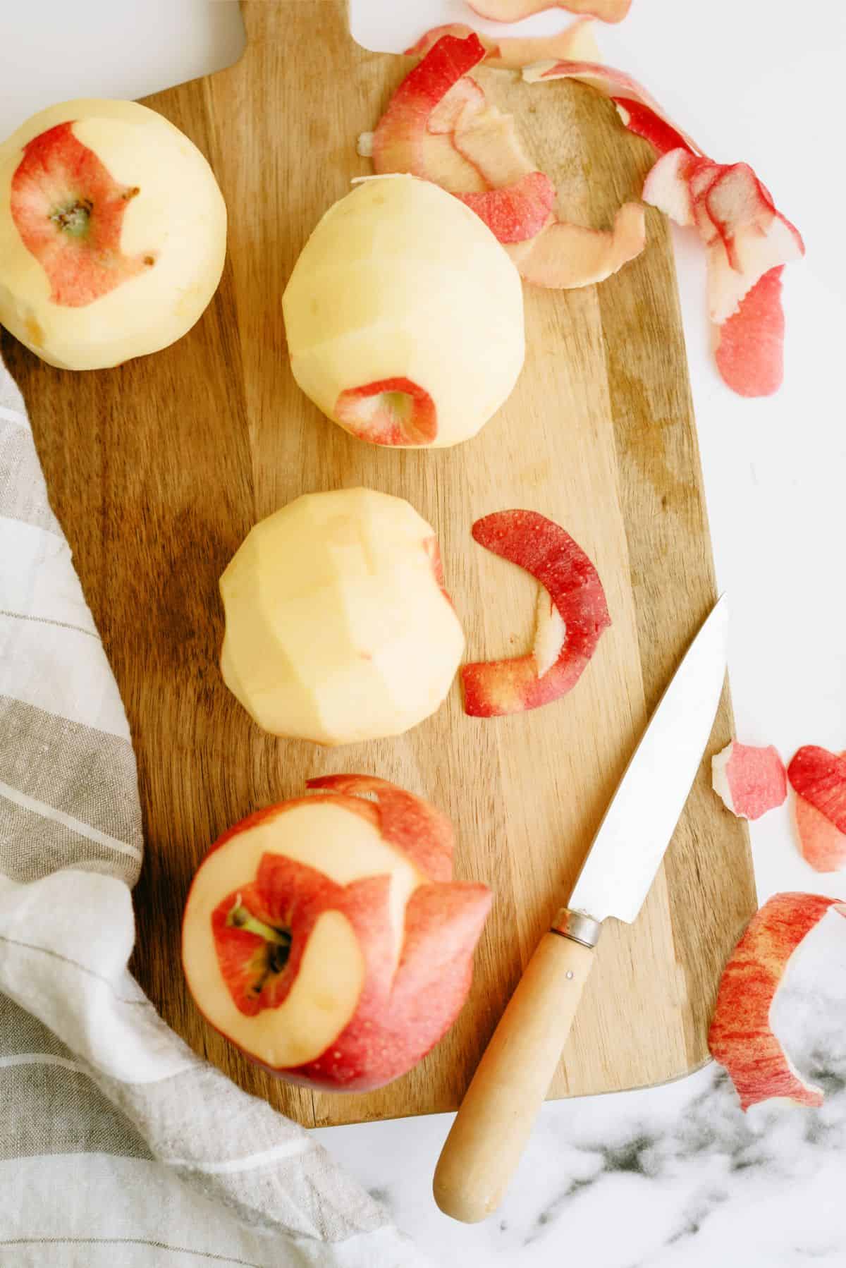 Peeled apples on a cutting board with a knife.