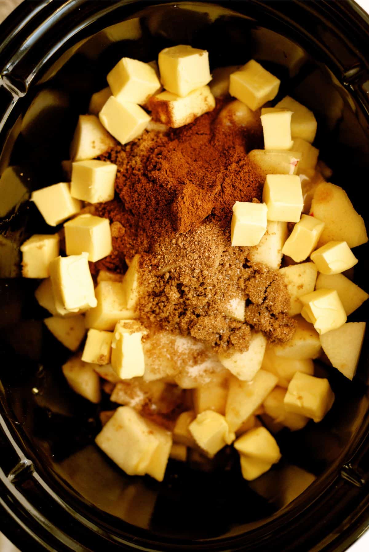 Cubed apples in the slow cooker topped with seasonings and cubed butter.