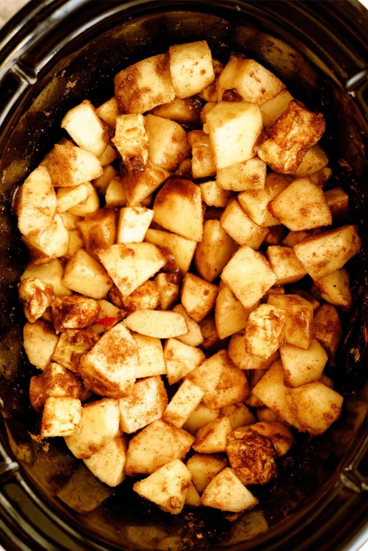 Uncooked cubed apples in the slow cooker covered with seasonings.