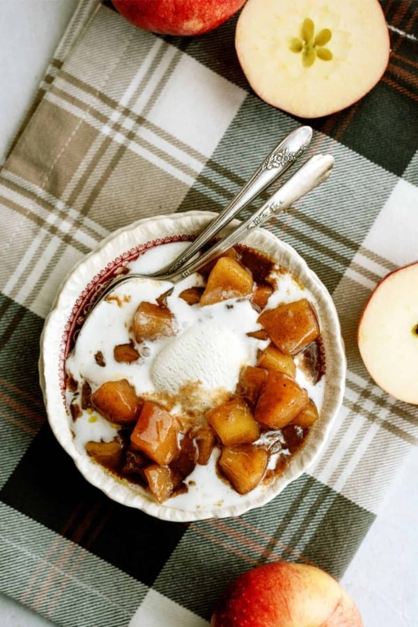 A bowl of cinnamon apples topped with vanilla ice cream with fresh cut apples around the bowl.