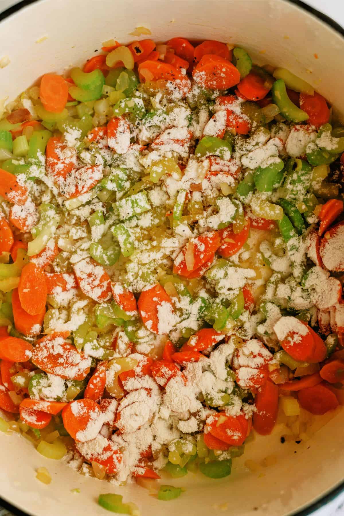 Flour sprinkled on top of chopped veggies in stock pot.