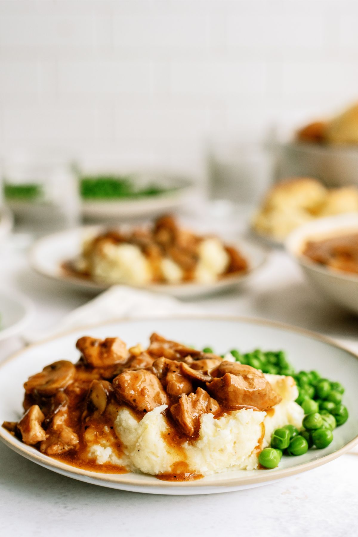 Plate of mashed potatoes topped with Instant Pot Pork Tips and Gravy with peas on the side