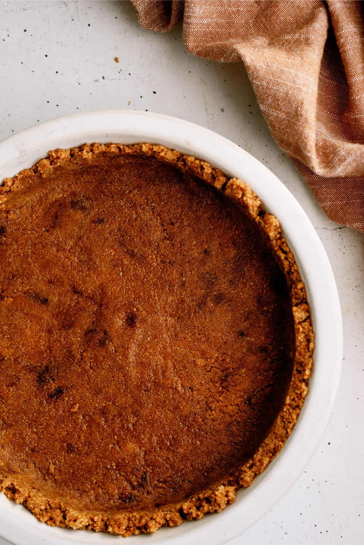 Top-down view of a baked pie in a white dish with a crumb crust, resting on a white surface next to a brown cloth.