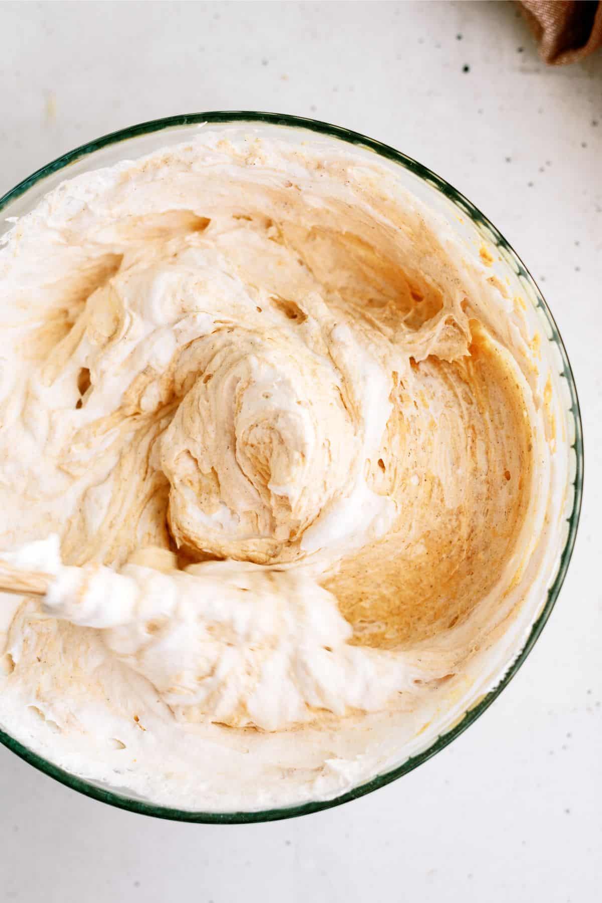 A glass bowl filled with a creamy, light brown mixture being stirred.