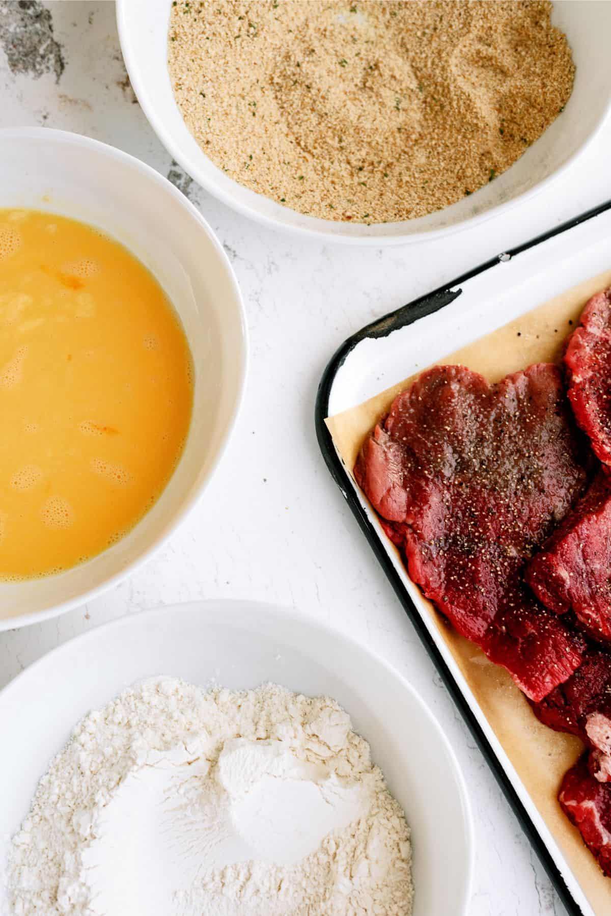 3 bowls (flour, eggs and bread crumbs)  for dipping and cube steak on a pan