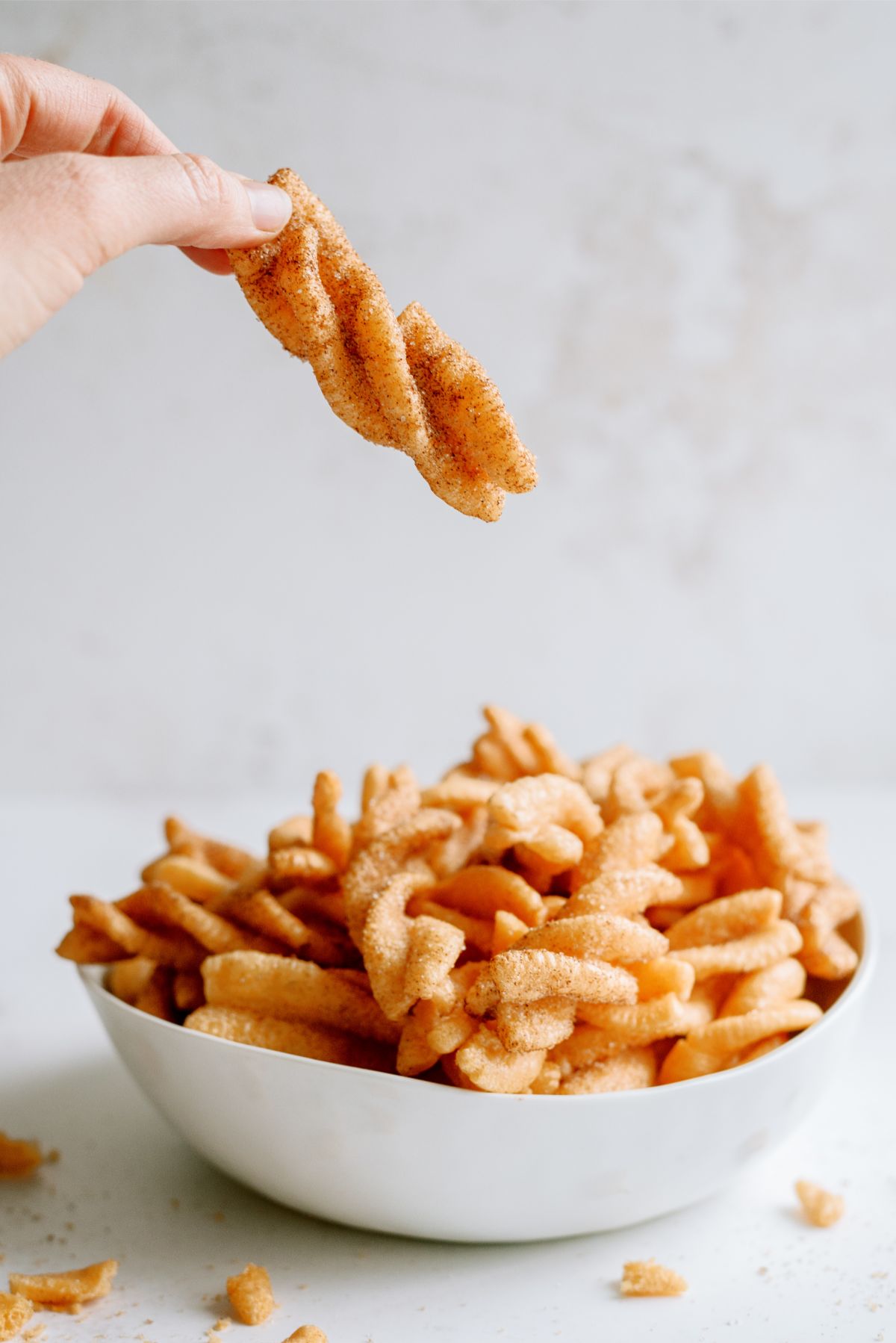 A bowl filled with Copycat Taco Bell Cinnamon Twists with one lifted by a hand