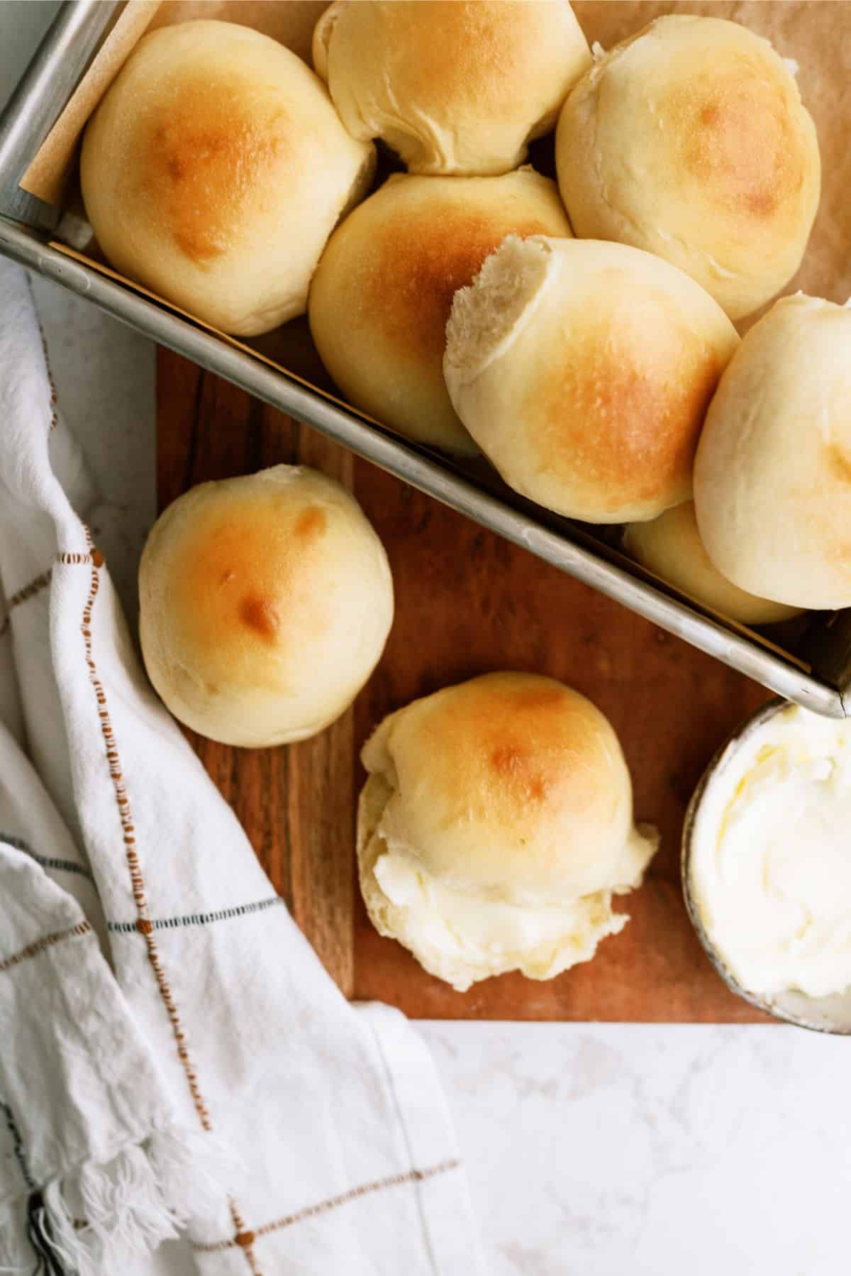 A pan of Homemade Potato Rolls with one opened and butter in the center of it