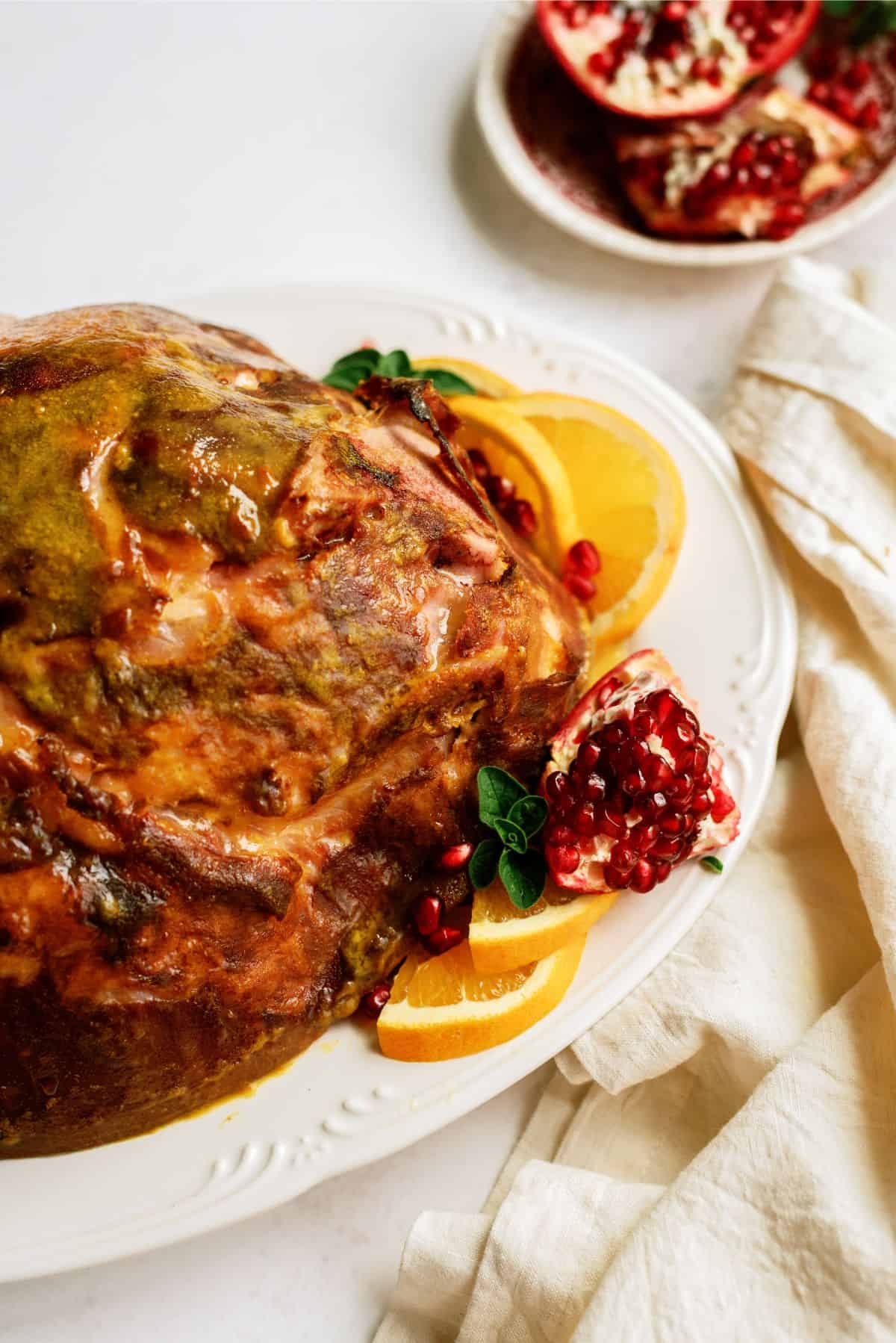 Roasted Ham Shank on a serving platter with pomegranate in the background