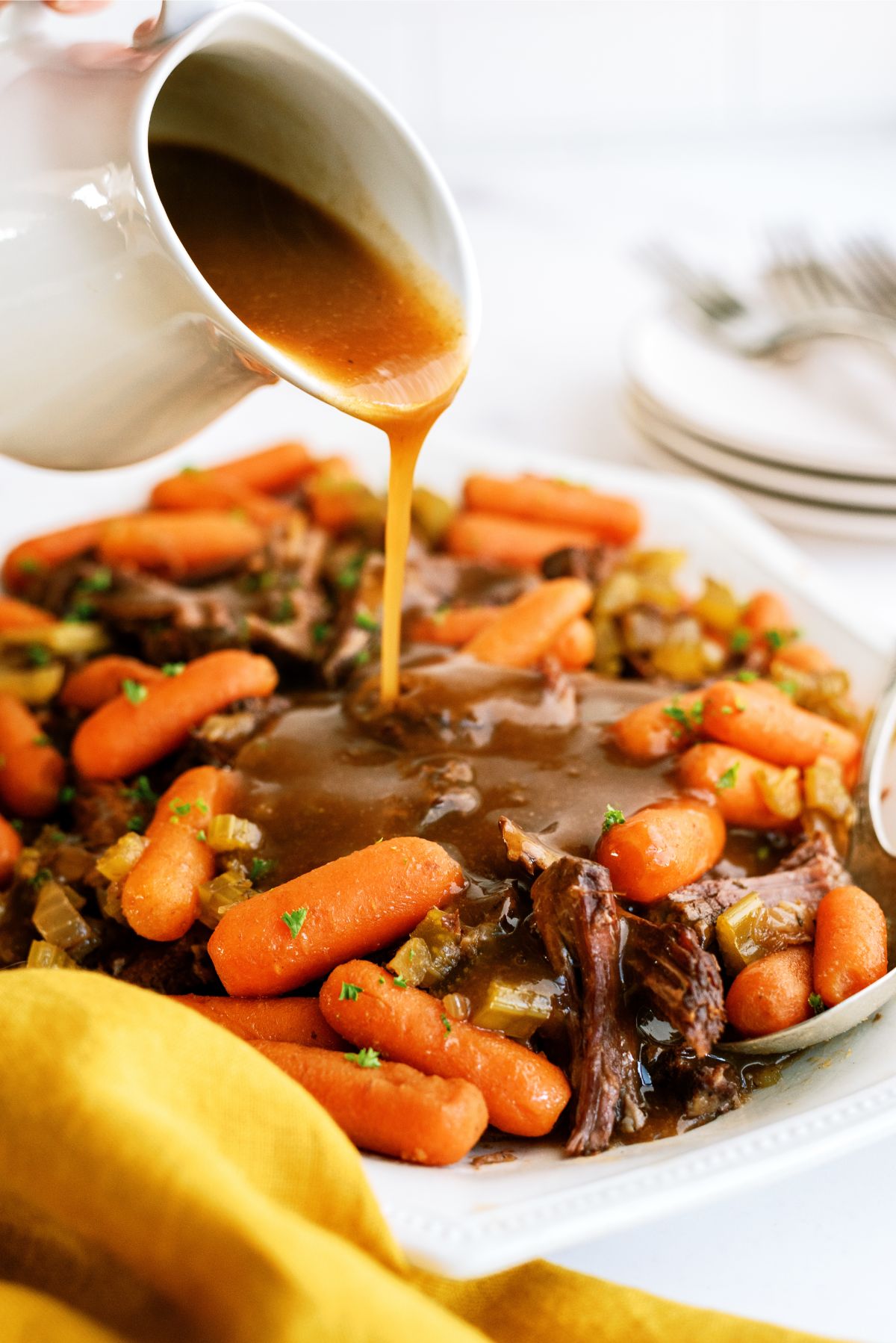 Pouring gravy on top of shredded Slow Cooker Balsamic Pot Roast on a serving plate