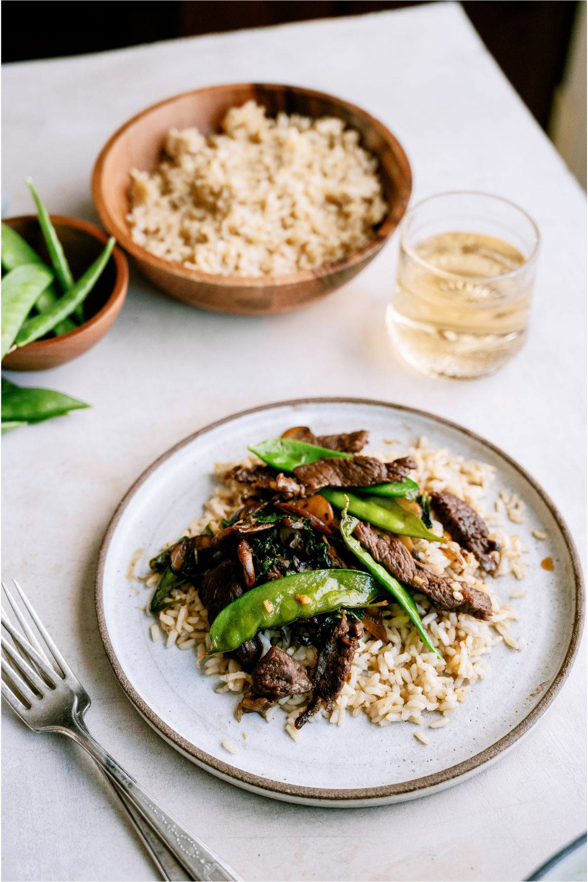 A plate of Asian Beef and Snow Peas served over rice with a bowl of rice in the background