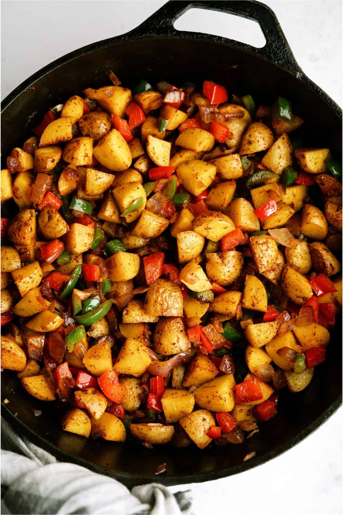 A skillet filled with diced, cooked potatoes mixed with diced red and green bell peppers, and onions.