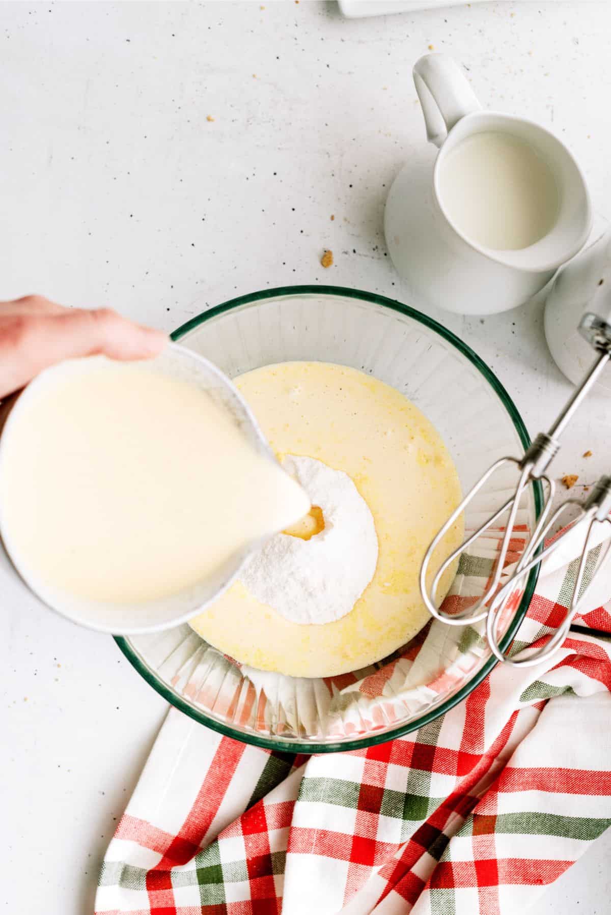 Pouring eggnog into pudding mixture inside a mixing bowl.