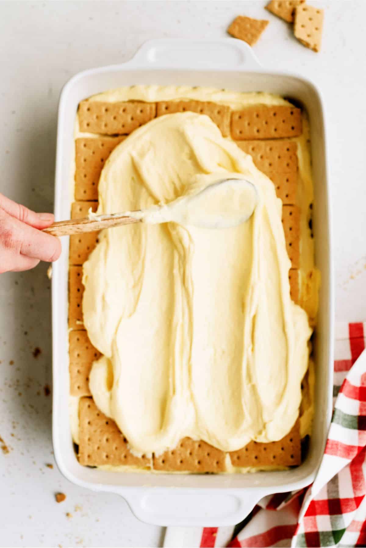Spreading eggnog pudding mixture over graham cracker sheets.