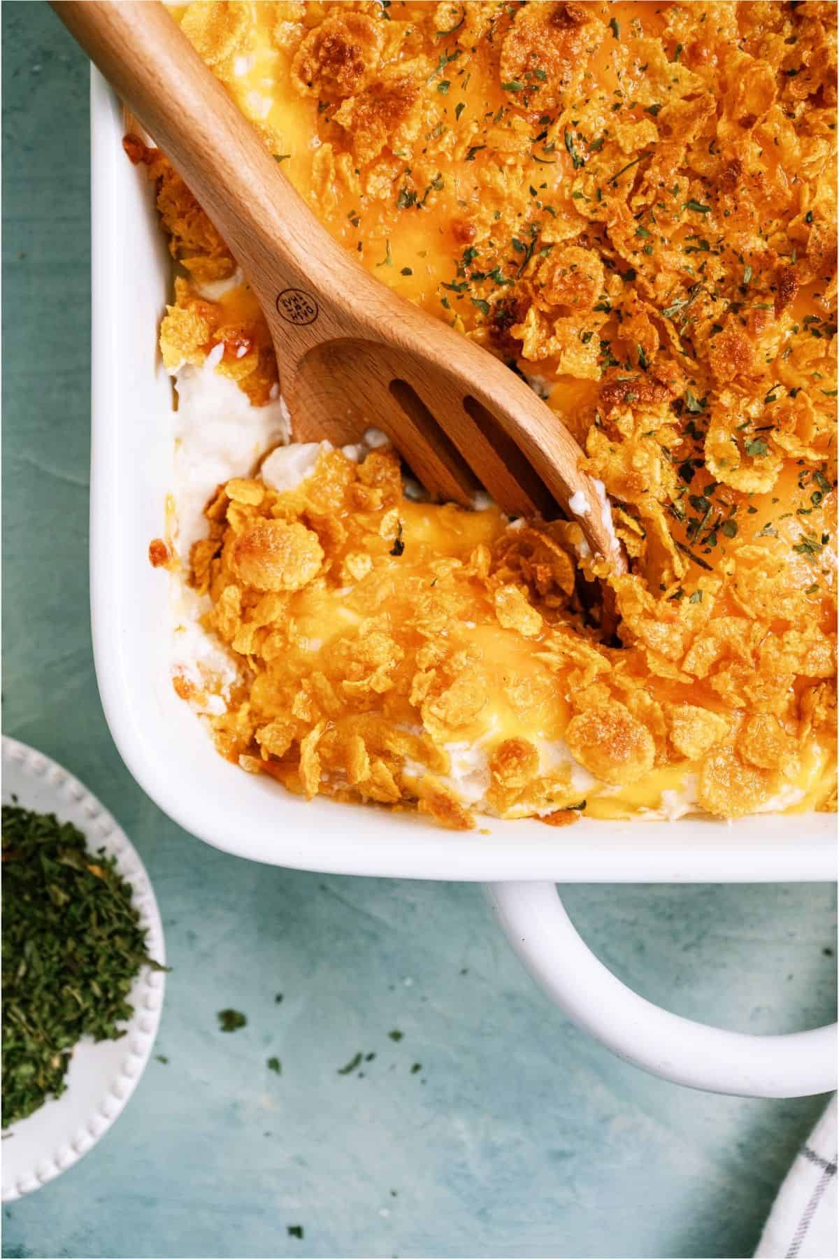 A wooden spoon scooping Funeral Potatoes {Cheesy Potato Casserole}.