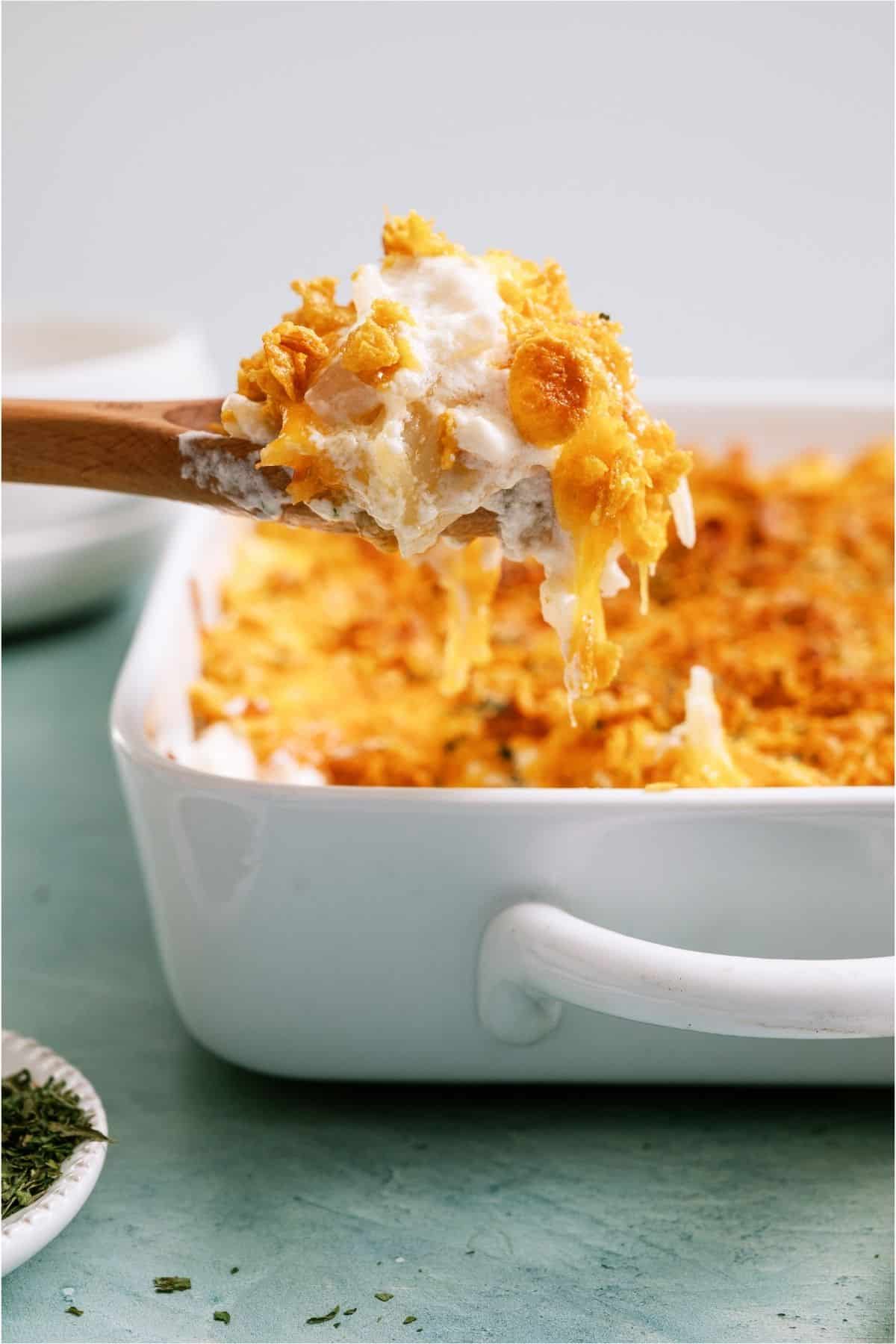 A scoop of Funeral Potatoes {Cheesy Potato Casserole} being held above the casserole.