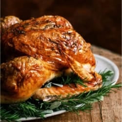 A roasted Turkey on a serving platter on top of a table.