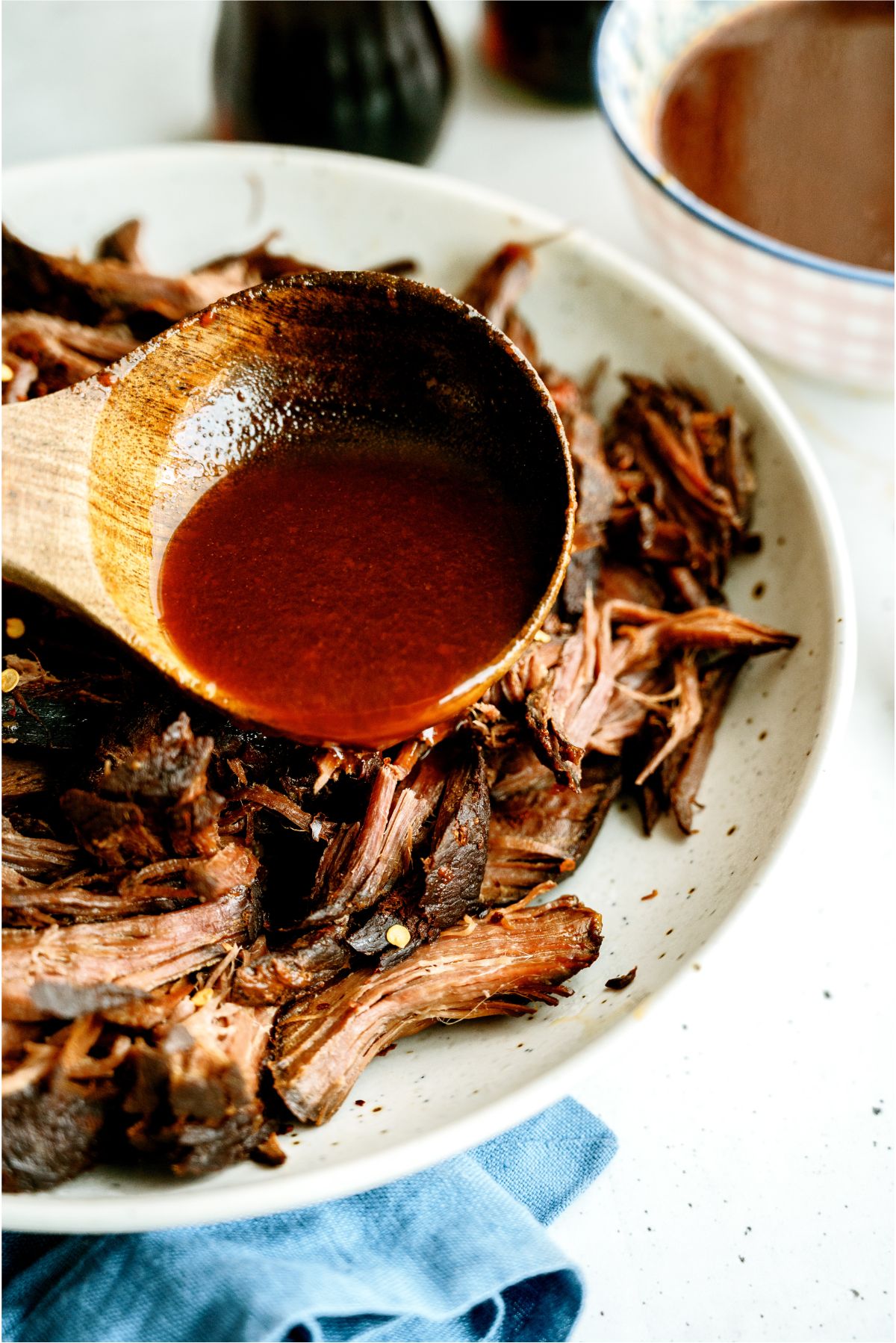 Spooning juices over Shredded Slow Cooker Cola BBQ Roast Beef on a serving plate