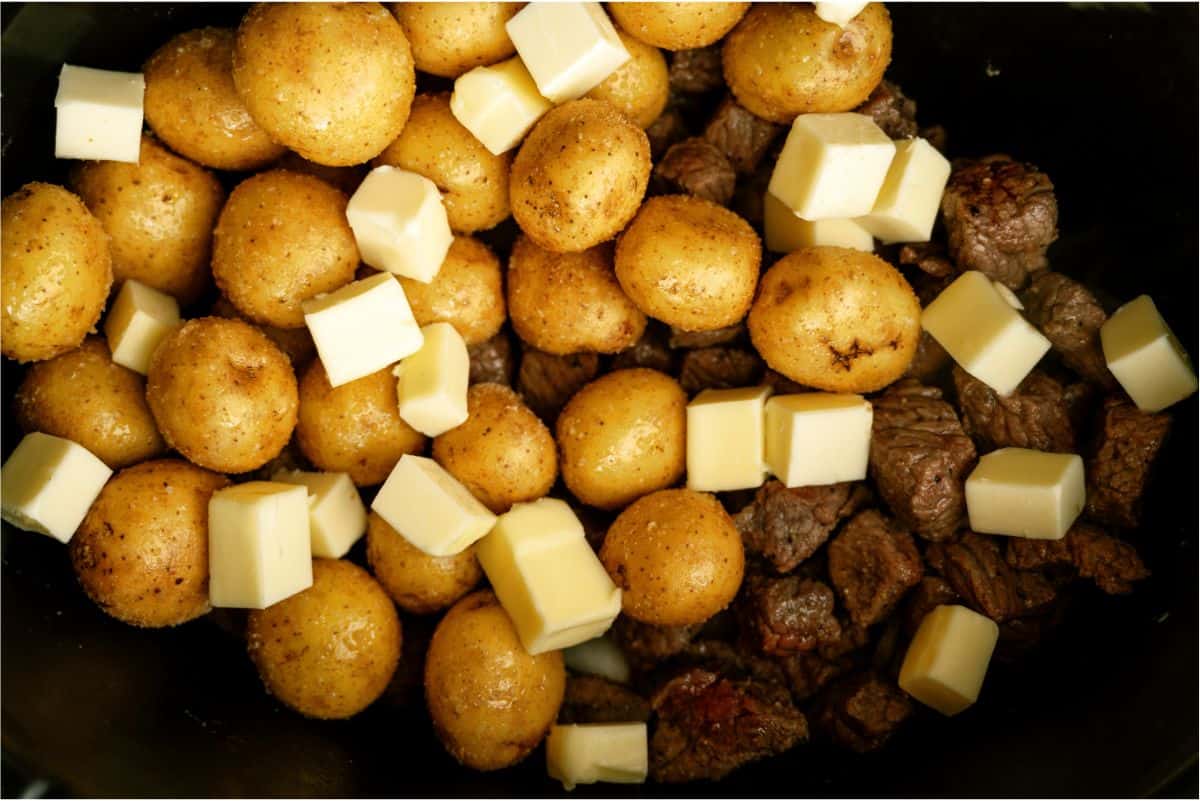 steak and potatoes in slow cooker with cubed butter on top