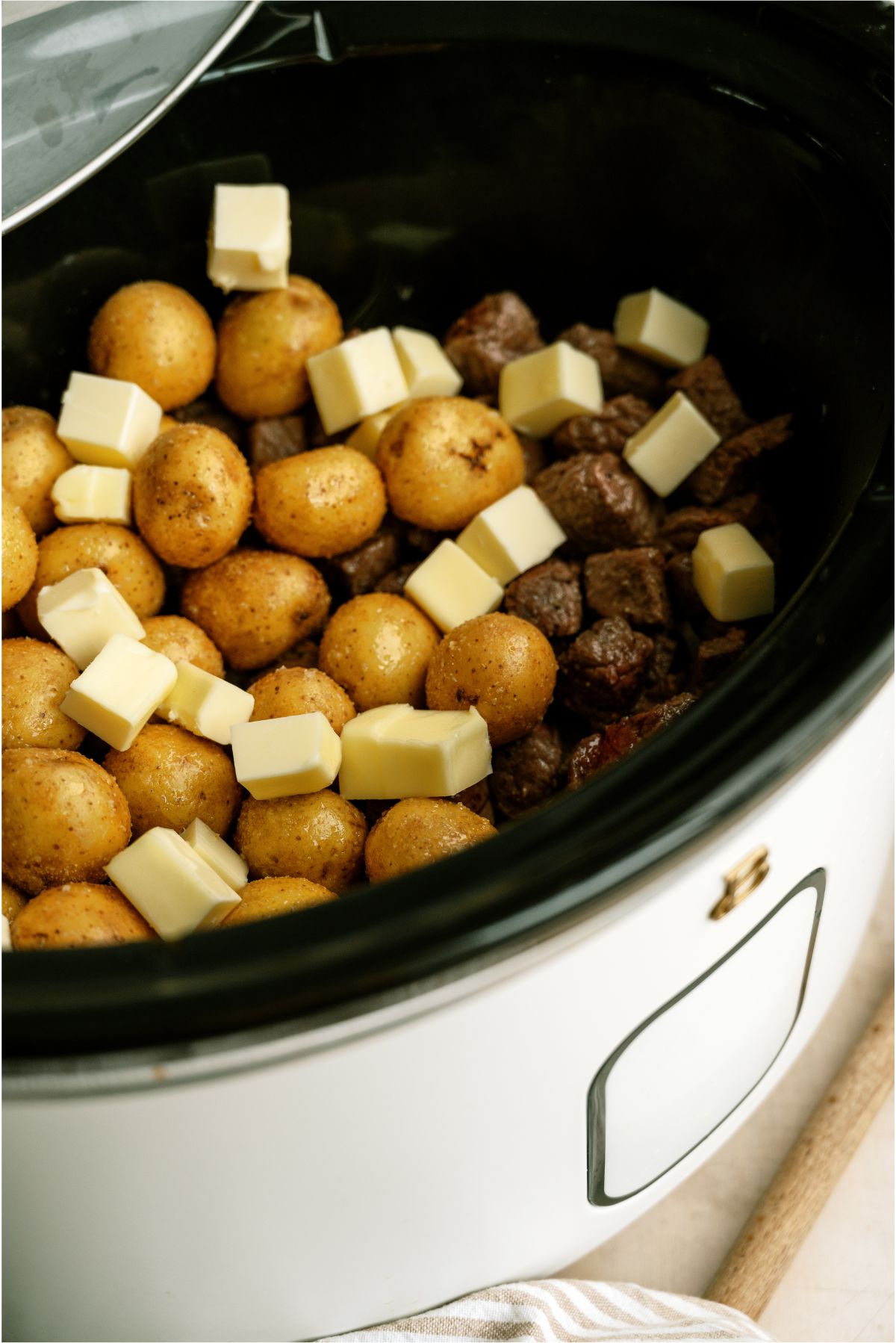 potatoes and steak with cubed butter on top in the slow cooker