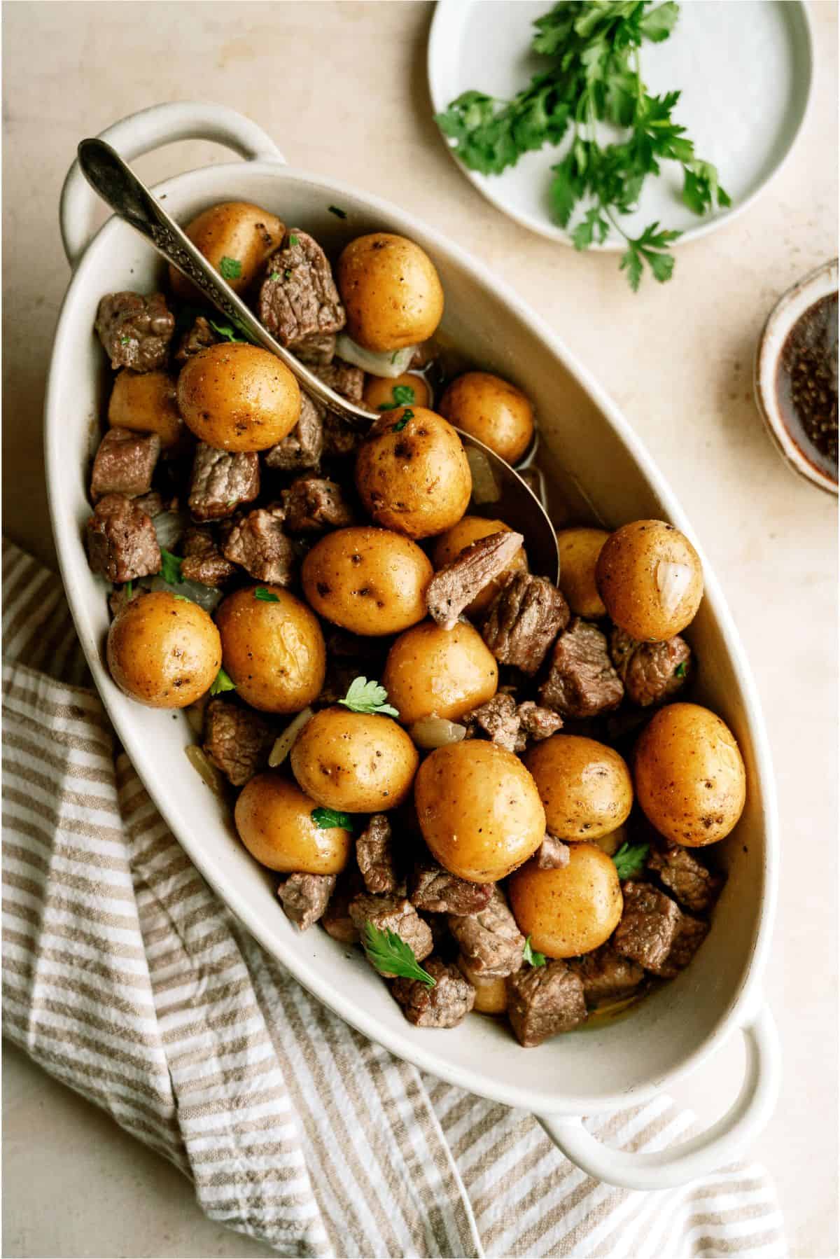 Slow Cooker Garlic Butter Steak and Potatoes in a serving dish with a serving spoon