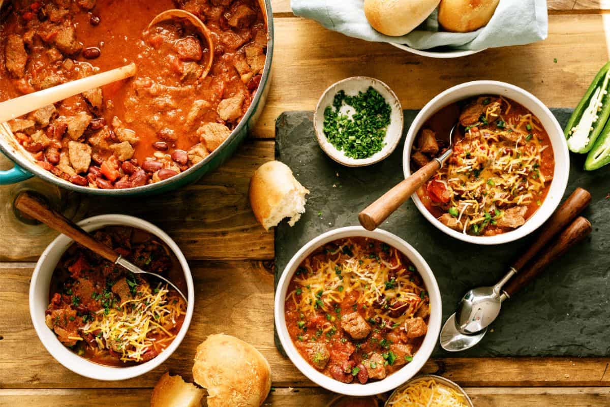 Large pot of Texas Roadhouse Copycat Chili with three seperate bowls full of Texas Roadhouse Copycat Chili and spoons