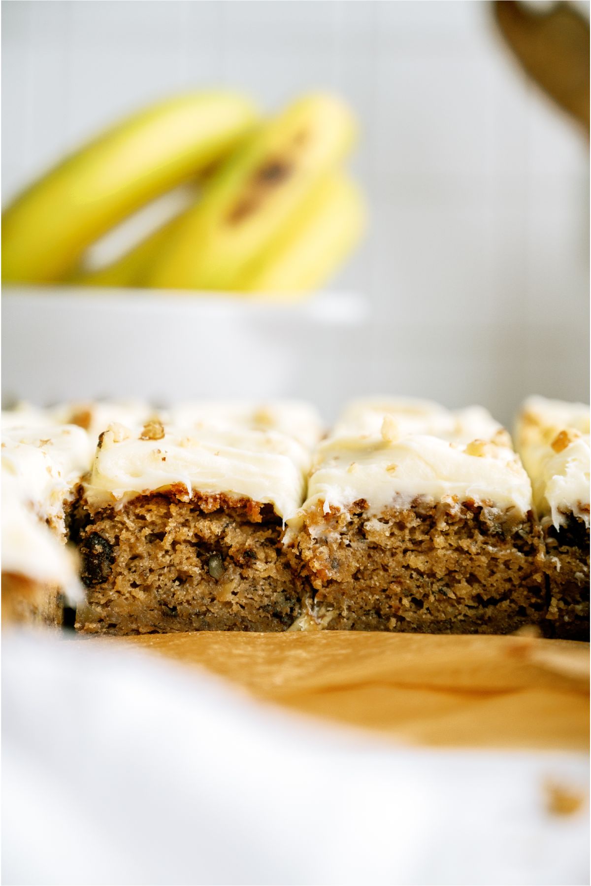Sliced Banana Bread Brownies with frosting with bananas in the background