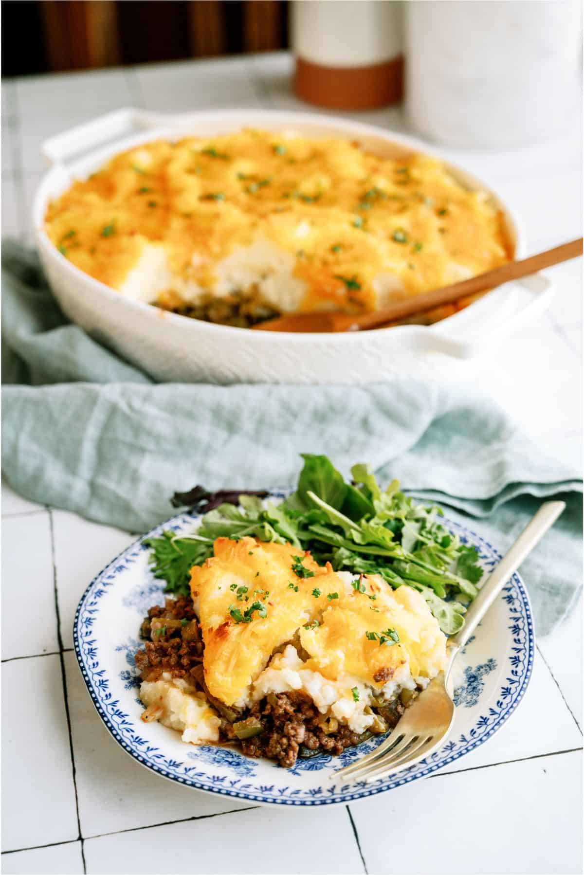 A serving of Bob Clark Casserole on a plate with the Bob Clark Casserole dish in the back