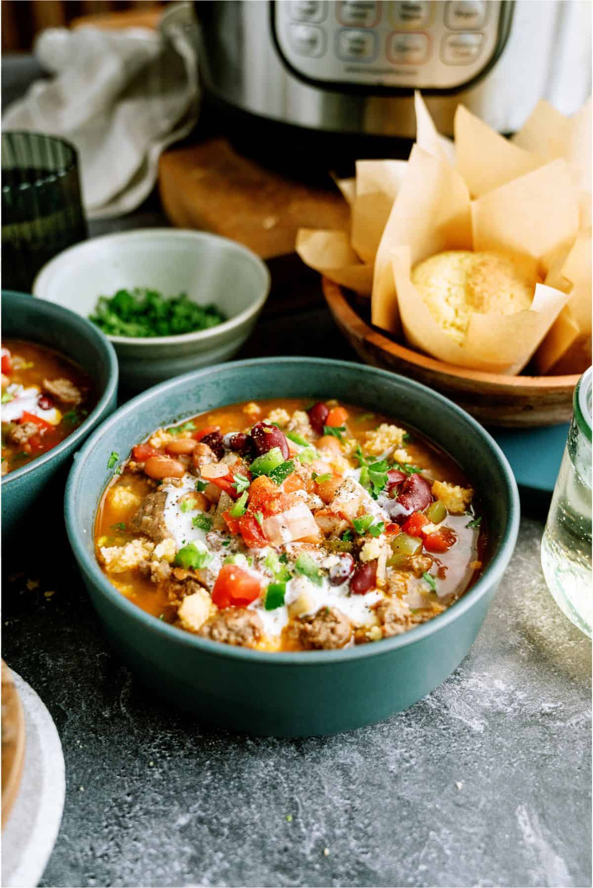 A bowl of Instant Pot Ground Turkey Chili with cornbread rolls in the background