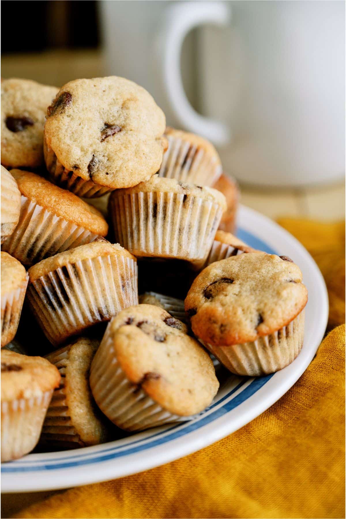 A plate filled with several mini banana chocolate chip muffins, with a white mug in the background.