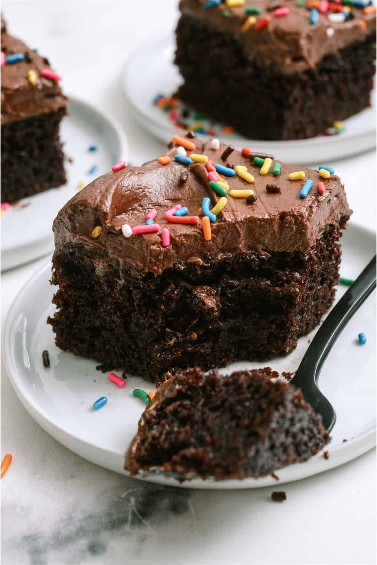 A slice of One Bowl Chocolate Cake on a plate with a fork slicing a bite out of it.