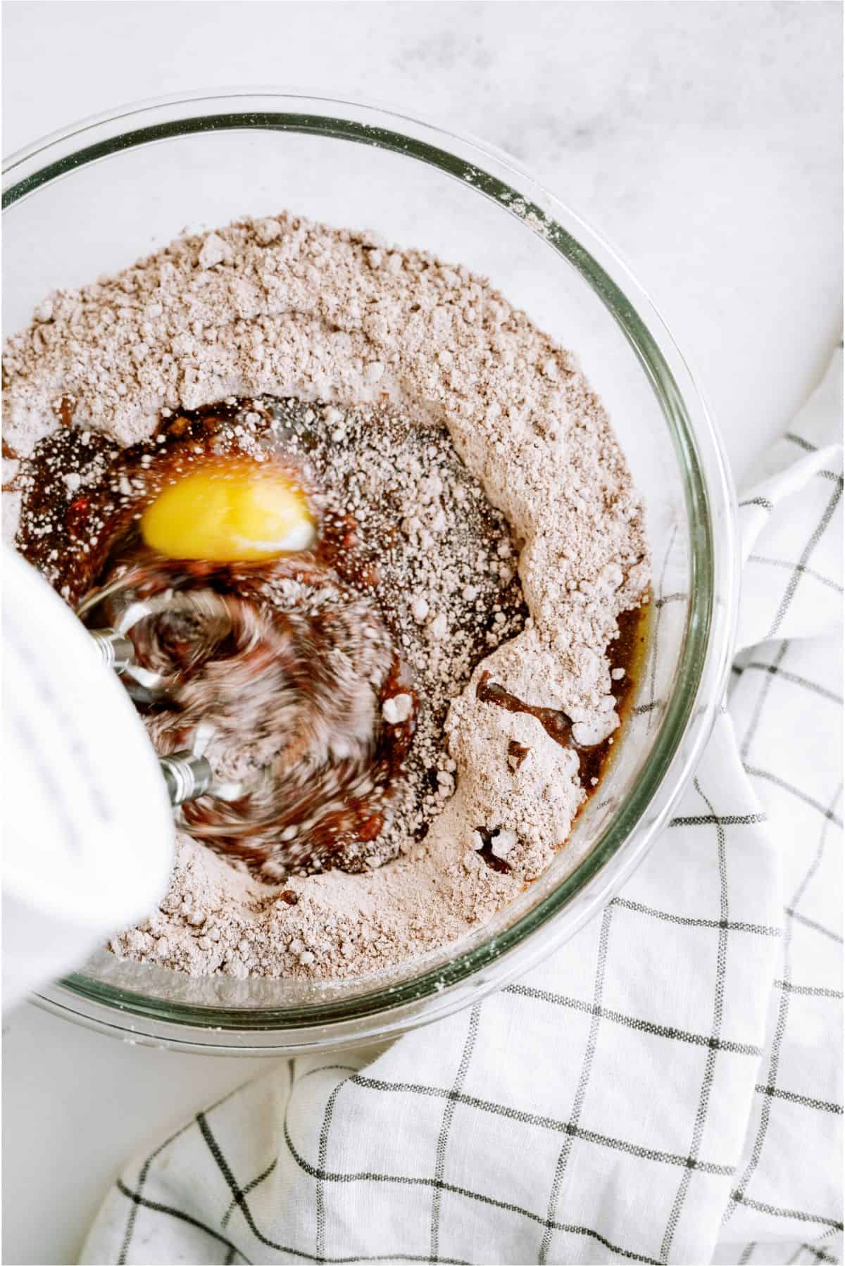A hand mixer mixing the ingredients for red velvet cookie dough in a glass bowl.