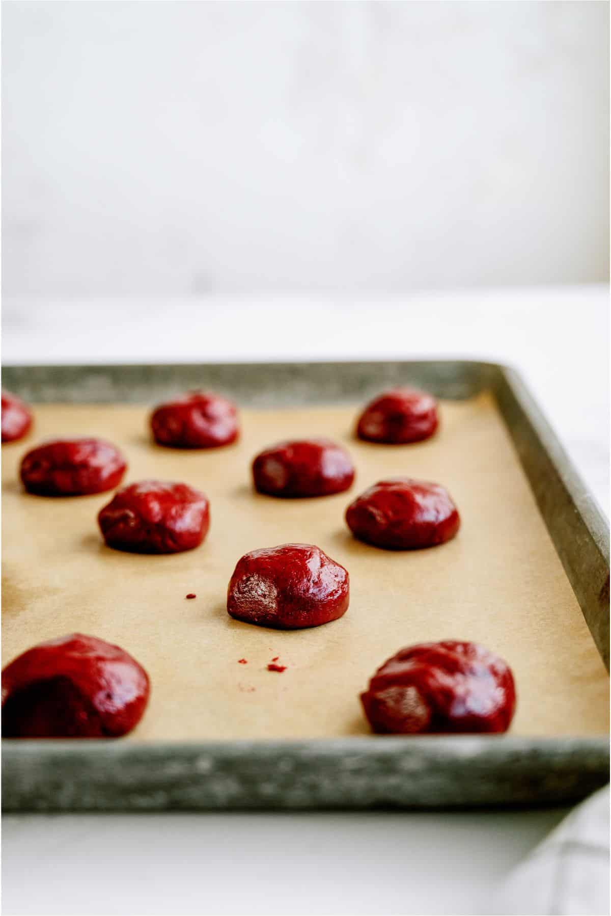 Red Velvet Cookie dough balls on a baking sheet lined with parchment paper.