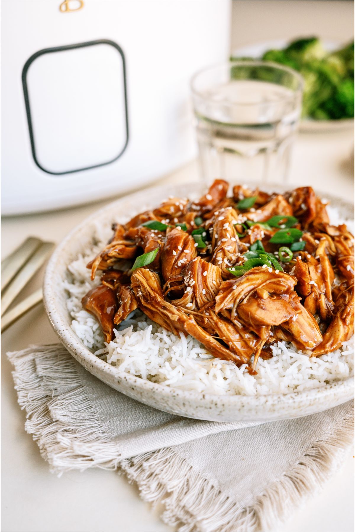 A plate of Slow Cooker Asian Glazed Chicken over rice with a slow cooker in the back ground