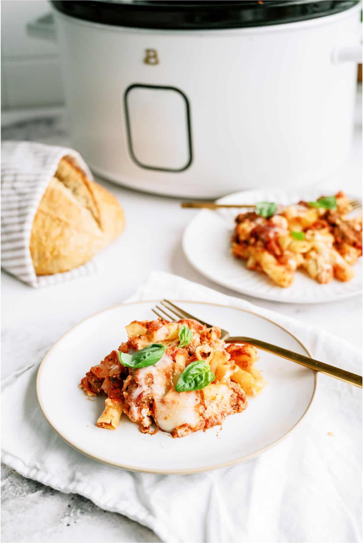 2 plates of Slow Cooker Baked Ziti in front of a slow cooker with french bread in the background