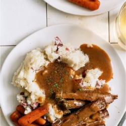 A plate of Slow Cooker Perfect Pot Roast and Homemade Gravy with mashed potatoes and carrots.