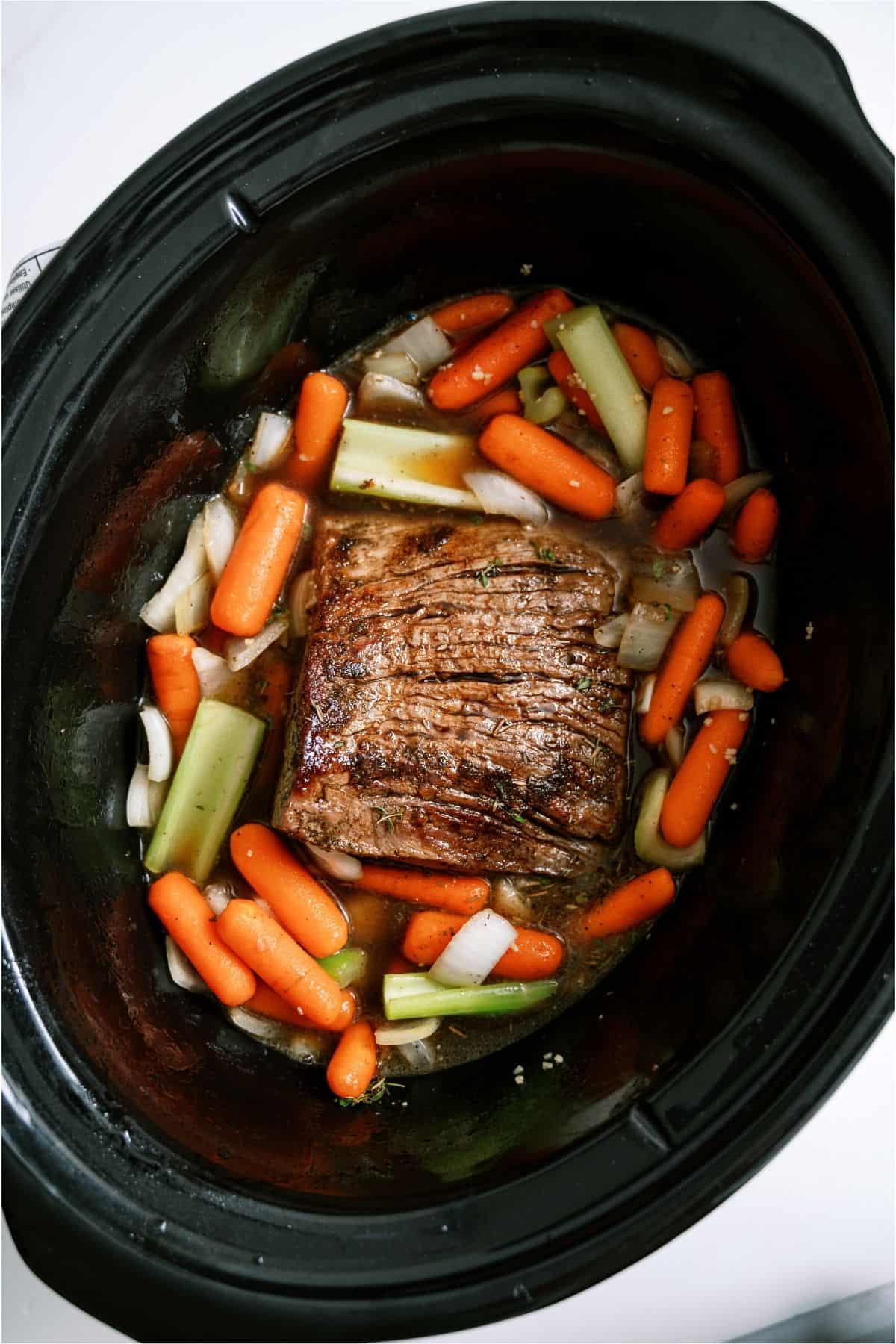 Slow cooker filled with a seared roast and veggies.