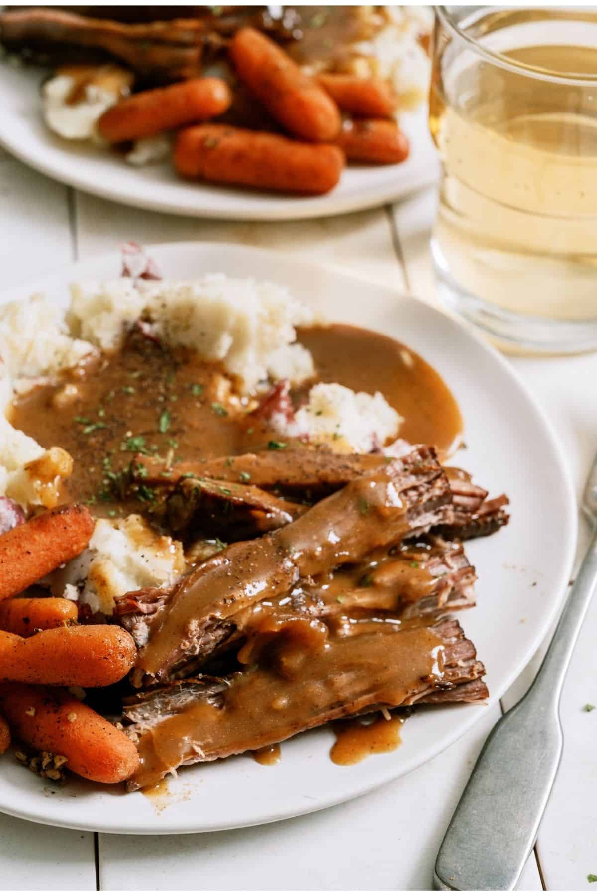 A plate with Slow Cooker Perfect Pot Roast and Homemade Gravy, mashed potatoes and carrots.