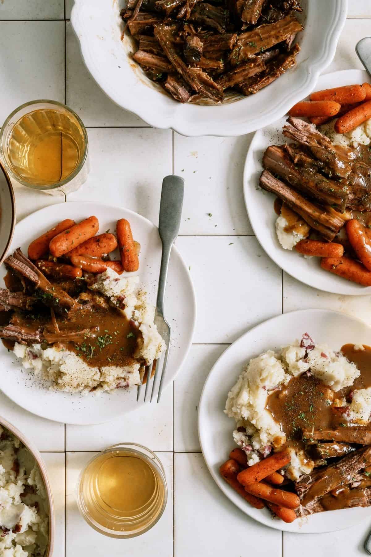 Plates filled with Slow Cooker Perfect Pot Roast and Homemade Gravy, mashed potatoes and carrots.