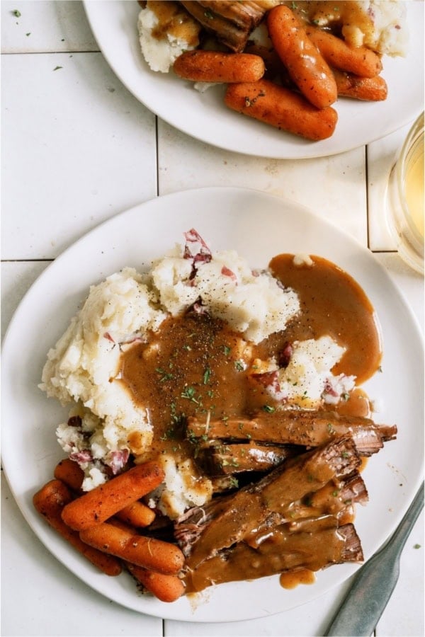 A plate of Slow Cooker Perfect Pot Roast and Homemade Gravy with mashed potatoes and carrots.